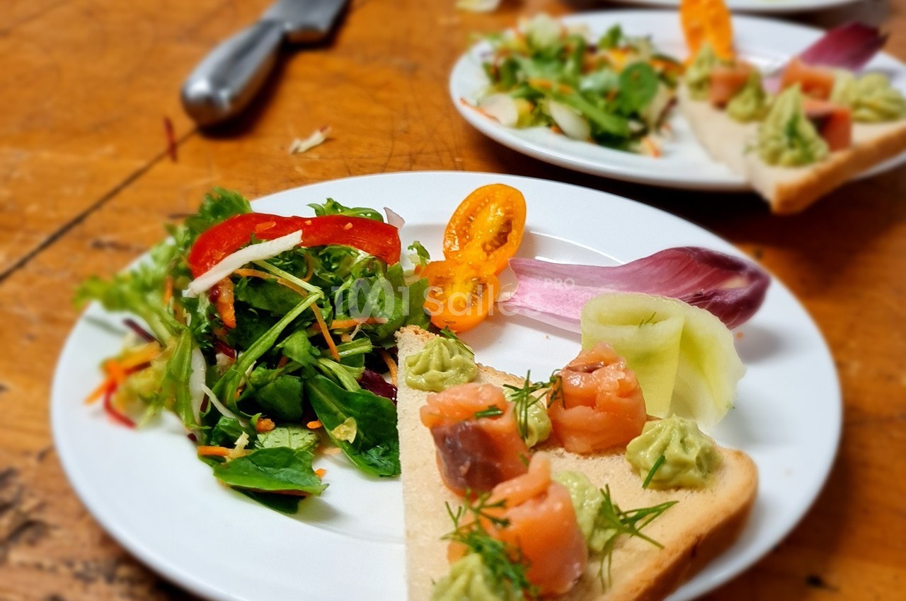 Assiette contenant une salade colorée et une tartine garnie de saumon, d'avocat et de légumes, sur une table en bois.