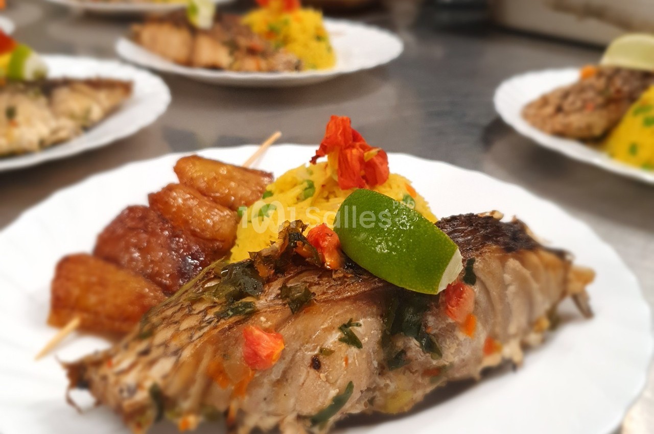 Assiette de poisson grillé avec herbes, plantains frits, riz safrané, garnie de fleurs comestibles et d'un quartier de…