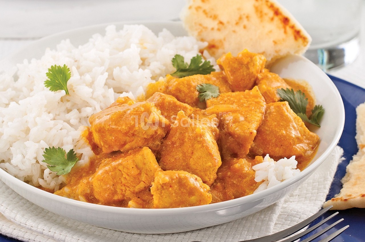 Assiette de poulet au curry avec riz blanc, garnie de coriandre, accompagnée de pain naan sur une table.