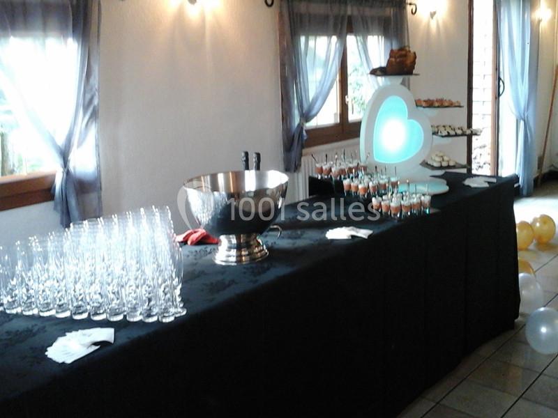 Table de réception avec verres alignés, coupe en métal, desserts sur présentoir et décorations lumineuses.