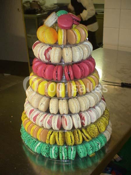 Tour de macarons colorés empilés sur un présentoir transparent dans une cuisine.