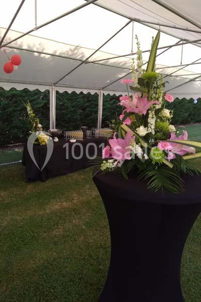Arrangement floral sur une table haute noire en extérieur, avec buffet en arrière-plan sous une tente blanche.