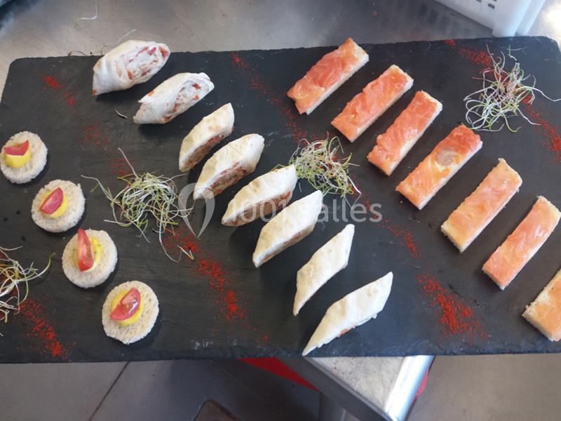 Plateau de bouchées apéritives variées avec roulés, toasts au saumon et canapés garnis, décoré de pousses vertes.