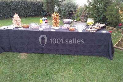 Table de buffet dressée en extérieur avec boissons, verrines, desserts et une pièce montée sur une nappe noire.