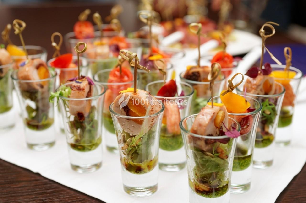 Verrines garnies de brochettes de viande et légumes colorés, présentées sur une table pour un buffet.
