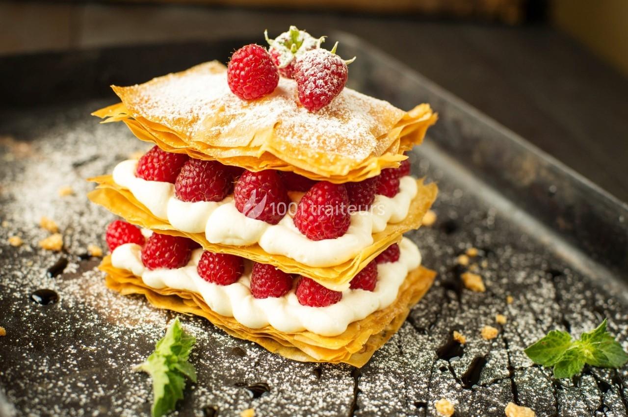 Millefeuille croustillant garni de crème fouettée et de framboises fraîches, saupoudré de sucre glace.