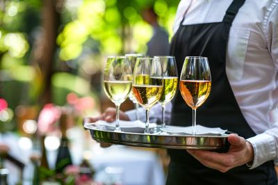 Un serveur portant un plateau avec des flûtes de champagne lors d'un événement en extérieur sous des arbres.