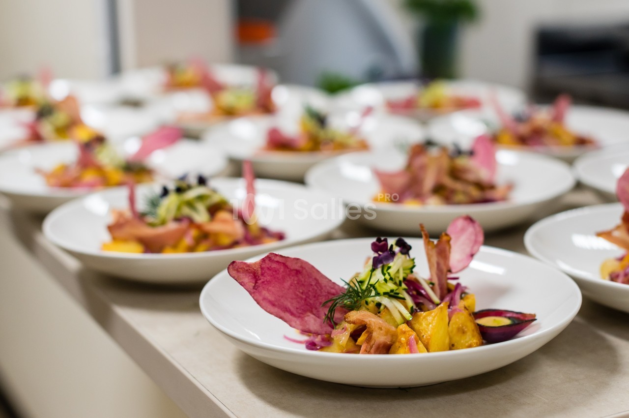 Assiettes de plats colorés avec légumes, chips de betterave et herbes fraîches alignées sur un plan de travail.
