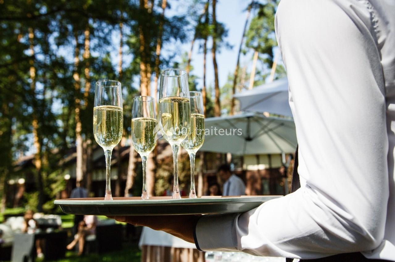 Un serveur portant un plateau avec des flûtes de champagne lors d'un événement en extérieur sous des arbres.