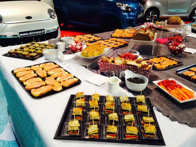 Buffet avec divers amuse-bouches, sandwichs, légumes et pains, disposés sur des nappes blanches et grises.