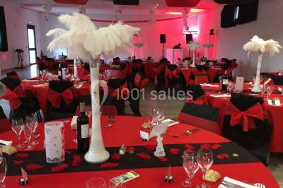 Centre de table floral avec roses et magnolias, bouteille de vin, numéro de table et décorations sur une nappe blanche.