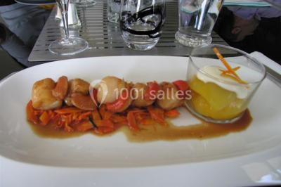 Centre de table floral avec roses et magnolias, bouteille de vin, numéro de table et décorations sur une nappe blanche.