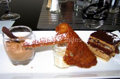 Centre de table floral avec roses et magnolias, bouteille de vin, numéro de table et décorations sur une nappe blanche.
