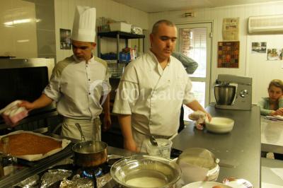 Centre de table floral avec roses et magnolias, bouteille de vin, numéro de table et décorations sur une nappe blanche.