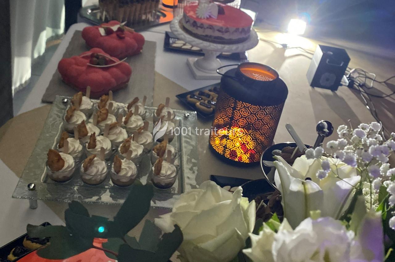 Table décorée avec des desserts variés, une lanterne allumée et des fleurs blanches au premier plan.