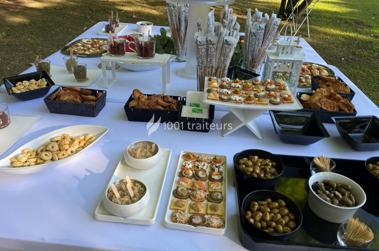 Buffet en plein air avec divers amuse-bouches, olives, biscuits salés et verrines disposés sur une table blanche.