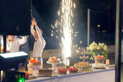 Centre de table floral avec roses et magnolias, bouteille de vin, numéro de table et décorations sur une nappe blanche.