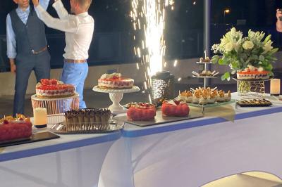 Centre de table floral avec roses et magnolias, bouteille de vin, numéro de table et décorations sur une nappe blanche.