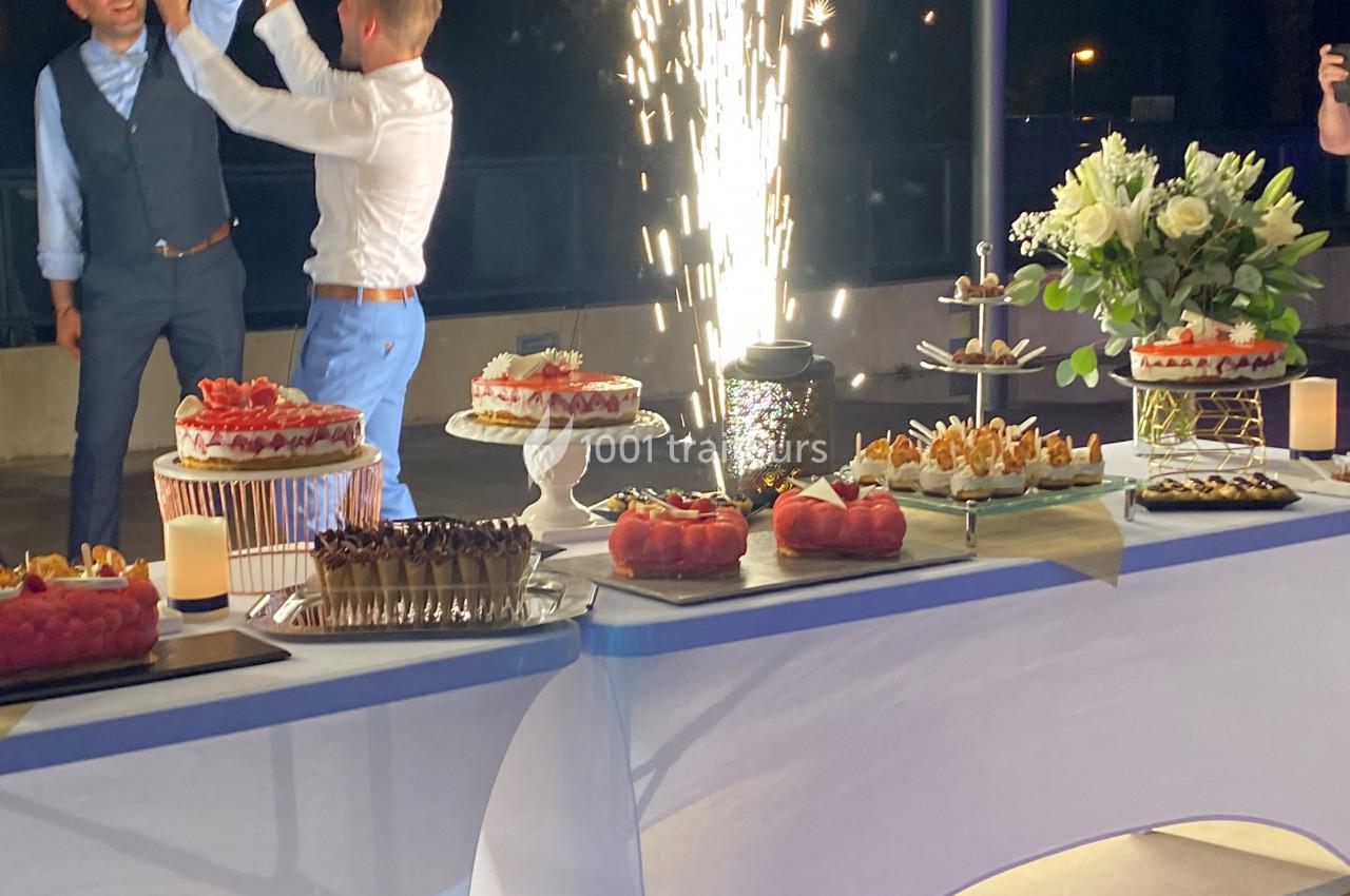 Table de desserts variés avec gâteaux, fleurs et fontaine lumineuse en arrière-plan lors d'une célébration nocturne.