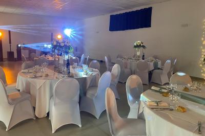 Centre de table floral avec roses et magnolias, bouteille de vin, numéro de table et décorations sur une nappe blanche.
