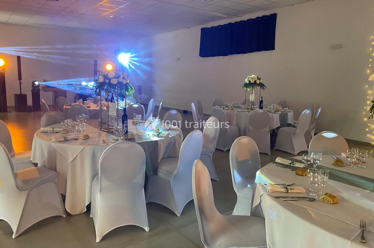 Salle de réception décorée avec des tables rondes, nappes blanches, chaises houssées et éclairage d'ambiance.