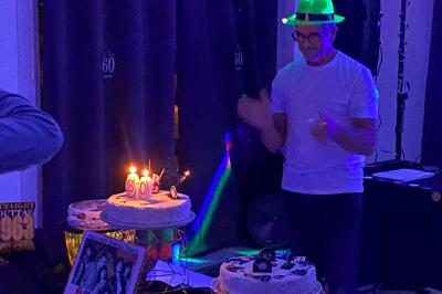 Centre de table floral avec roses et magnolias, bouteille de vin, numéro de table et décorations sur une nappe blanche.