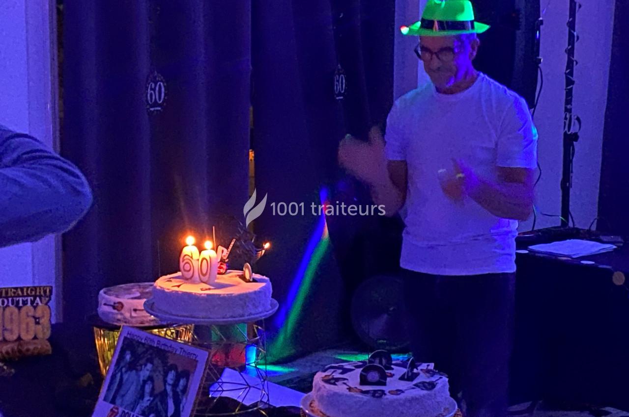 Un homme applaudit devant un gâteau d'anniversaire illuminé par des bougies dans une ambiance festive et tamisée.