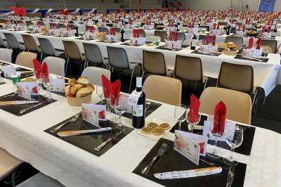 Centre de table floral avec roses et magnolias, bouteille de vin, numéro de table et décorations sur une nappe blanche.