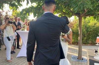 Centre de table floral avec roses et magnolias, bouteille de vin, numéro de table et décorations sur une nappe blanche.