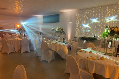 Centre de table floral avec roses et magnolias, bouteille de vin, numéro de table et décorations sur une nappe blanche.