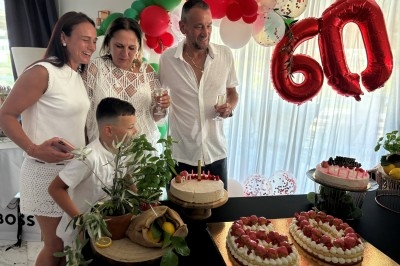 Centre de table floral avec roses et magnolias, bouteille de vin, numéro de table et décorations sur une nappe blanche.