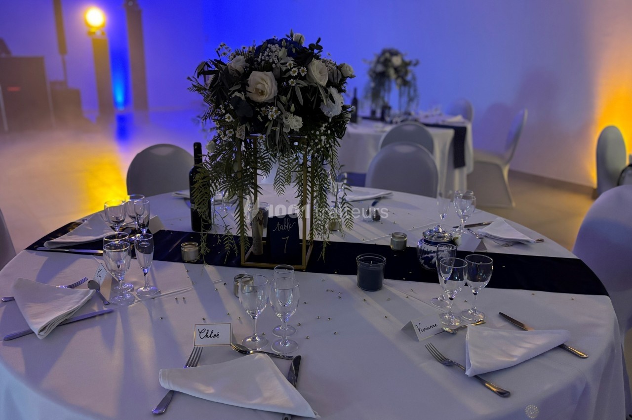 Table de réception élégamment dressée avec nappes blanches, centre de table floral et vaisselle disposée.