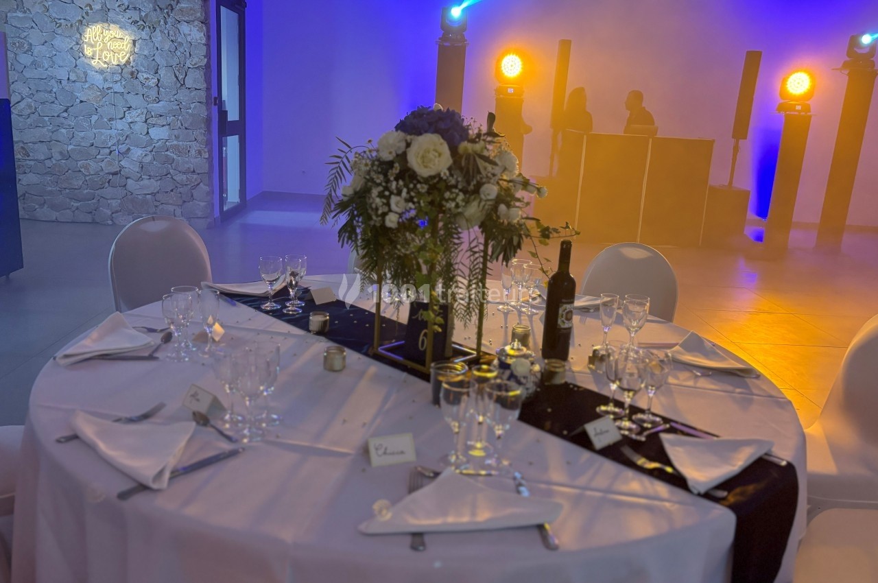 Table de réception élégamment dressée avec fleurs, vaisselle raffinée et éclairage d'ambiance en arrière-plan.