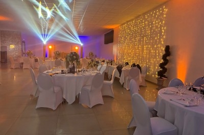 Centre de table floral avec roses et magnolias, bouteille de vin, numéro de table et décorations sur une nappe blanche.