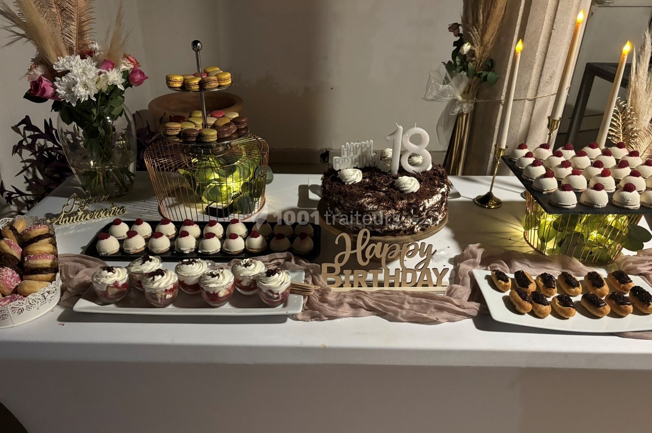 Table décorée pour un 18e anniversaire avec un gâteau au centre, cupcakes, macarons et autres pâtisseries.