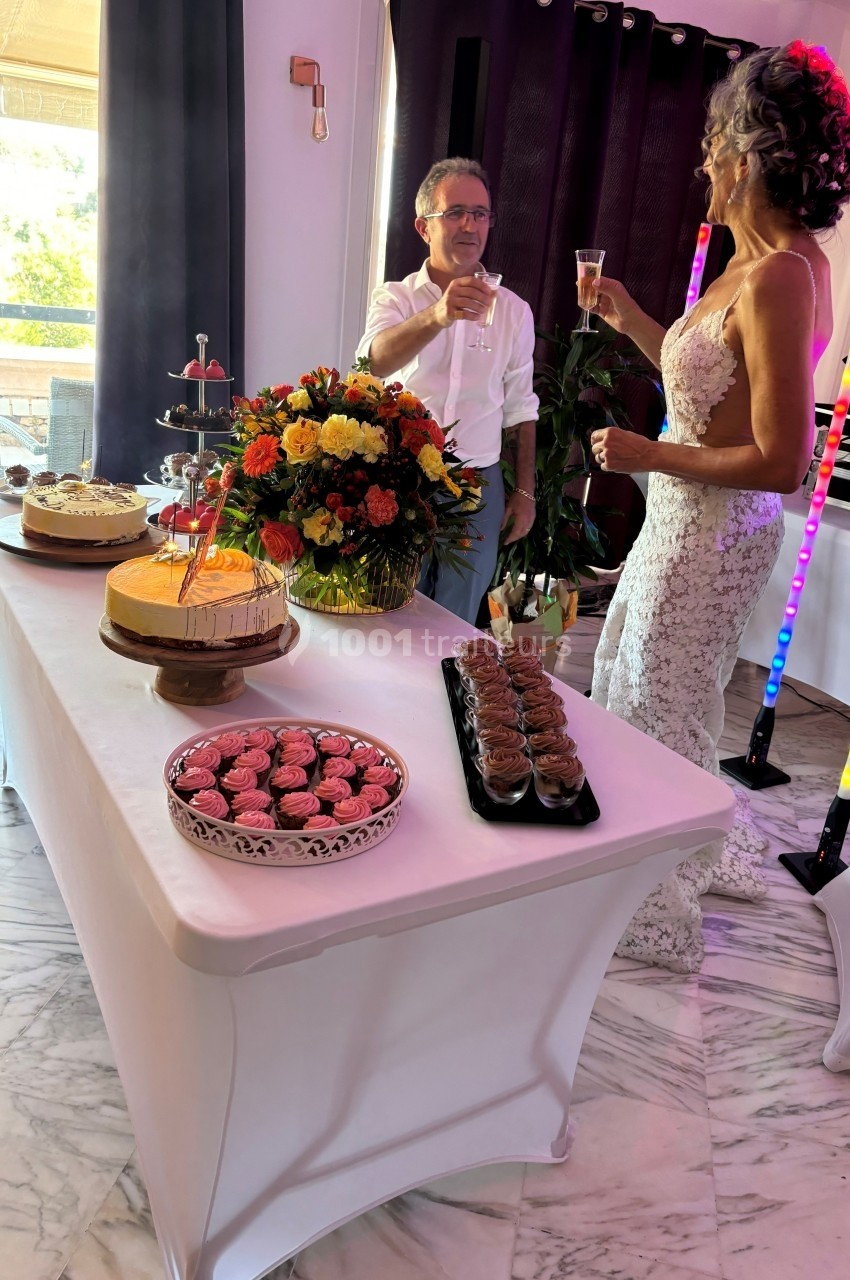 Un couple en tenue de mariage trinque près d'une table garnie de desserts et d'un bouquet de fleurs.