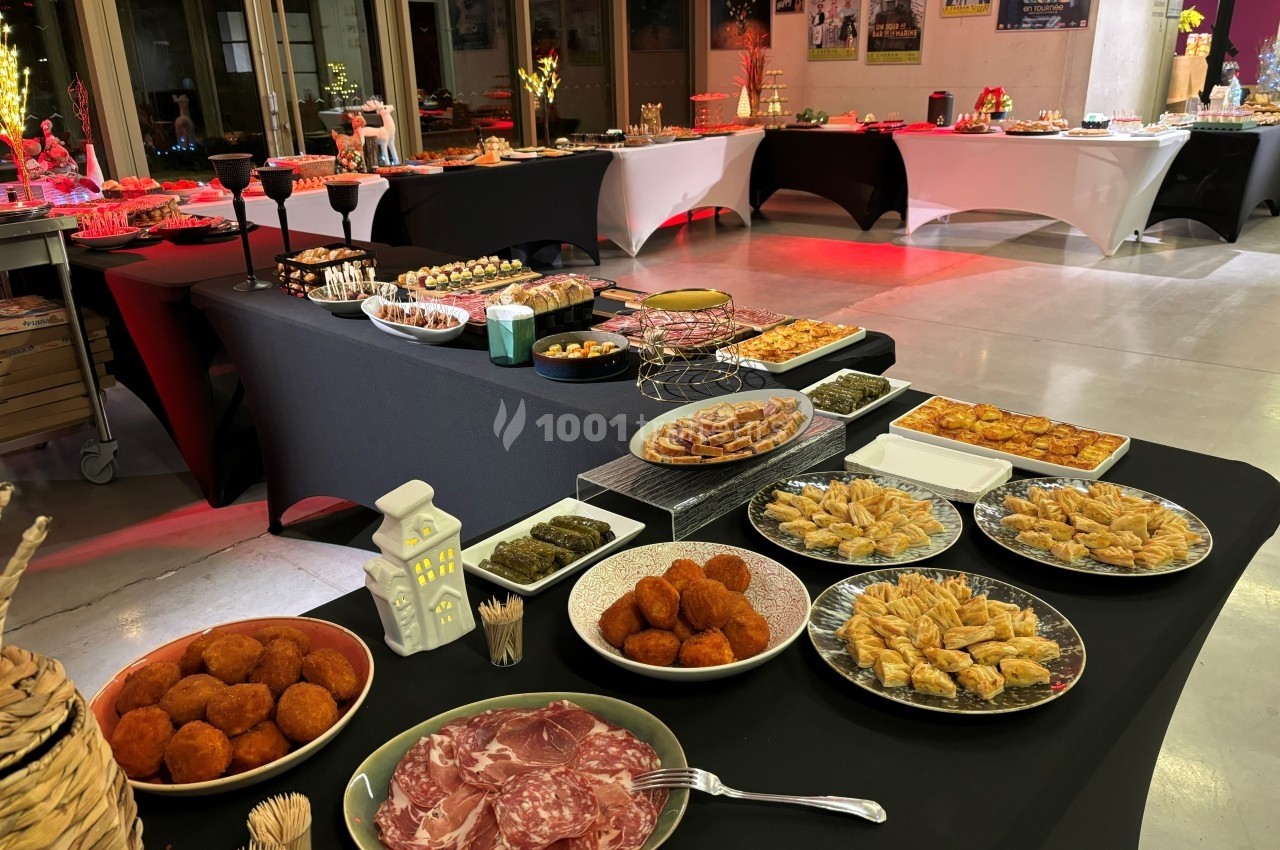 Buffet varié avec des plats salés et sucrés disposés sur des tables noires dans une salle éclairée.