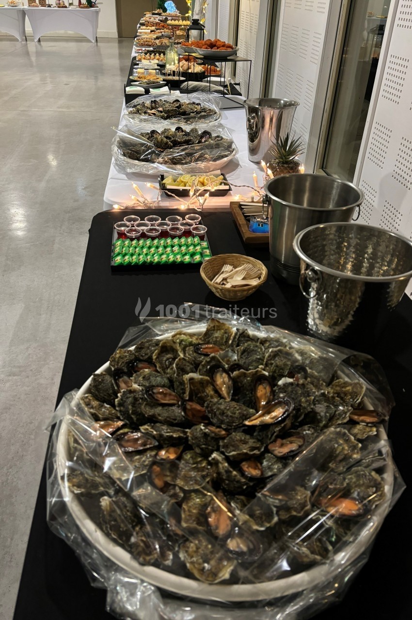 Buffet avec des plateaux d'huîtres, verrines et autres mets disposés sur une longue table dans une salle lumineuse.