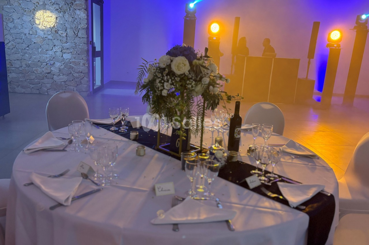Table de réception élégamment dressée avec fleurs, vaisselle raffinée et éclairage d'ambiance en arrière-plan.