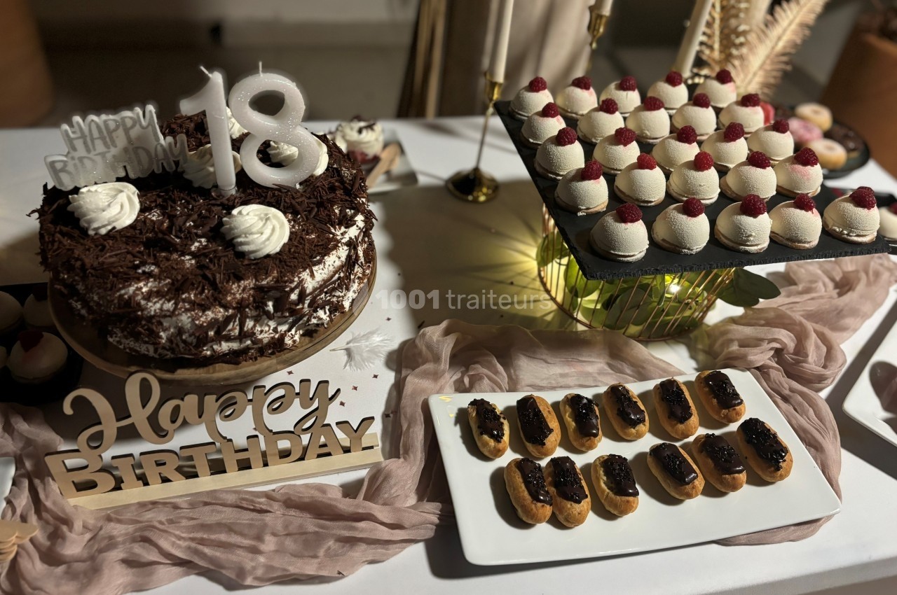 Table décorée pour un 18e anniversaire avec gâteau au chocolat, éclairs et mignardises garnies de framboises.