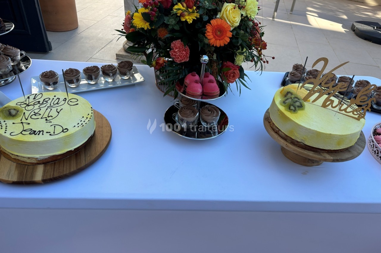 Deux gâteaux décorés pour un mariage, accompagnés de fleurs colorées et de desserts sur une table blanche.