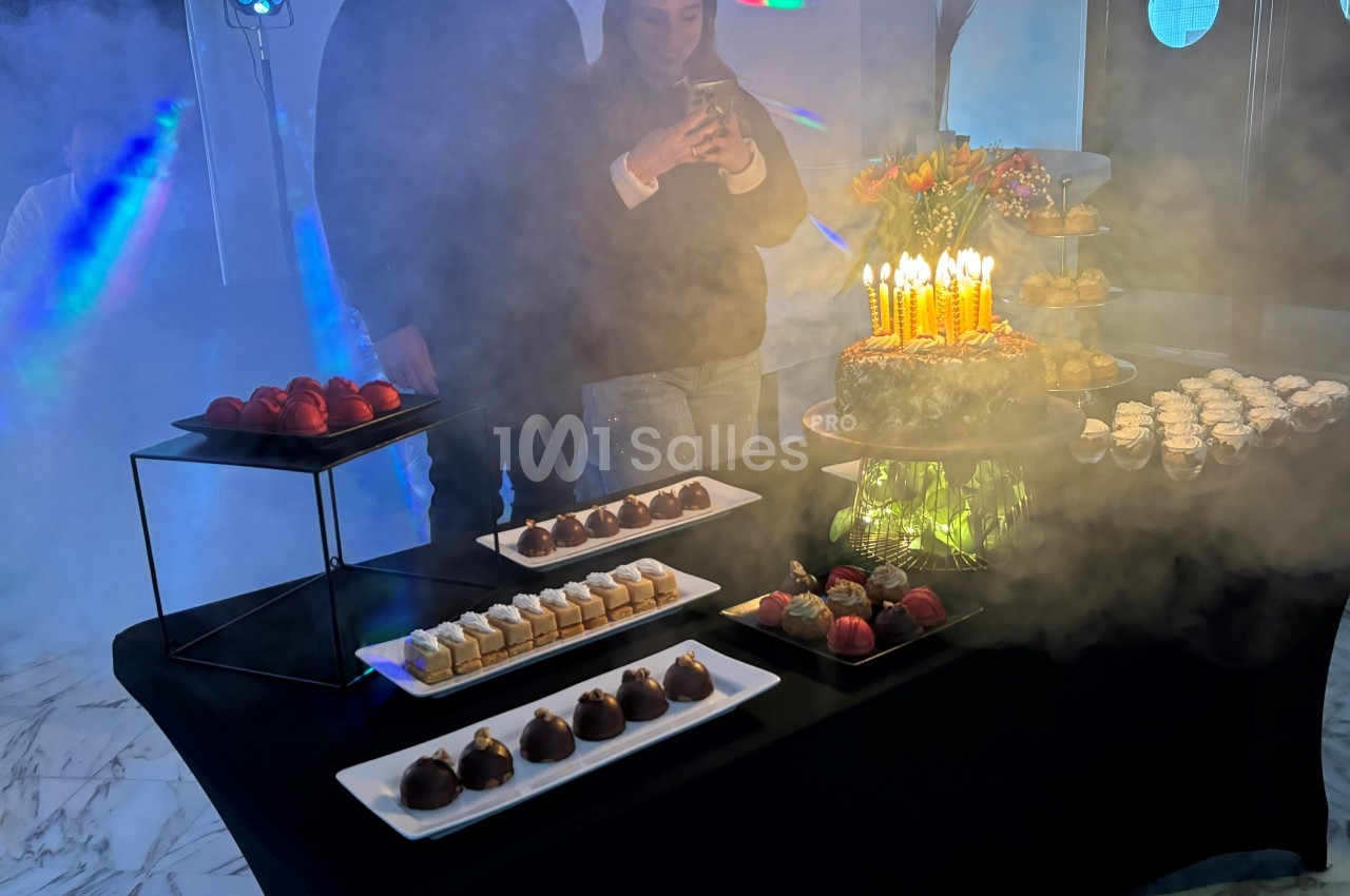 Table de desserts variés avec un gâteau d'anniversaire illuminé par des bougies, entourée de fumée légère.
