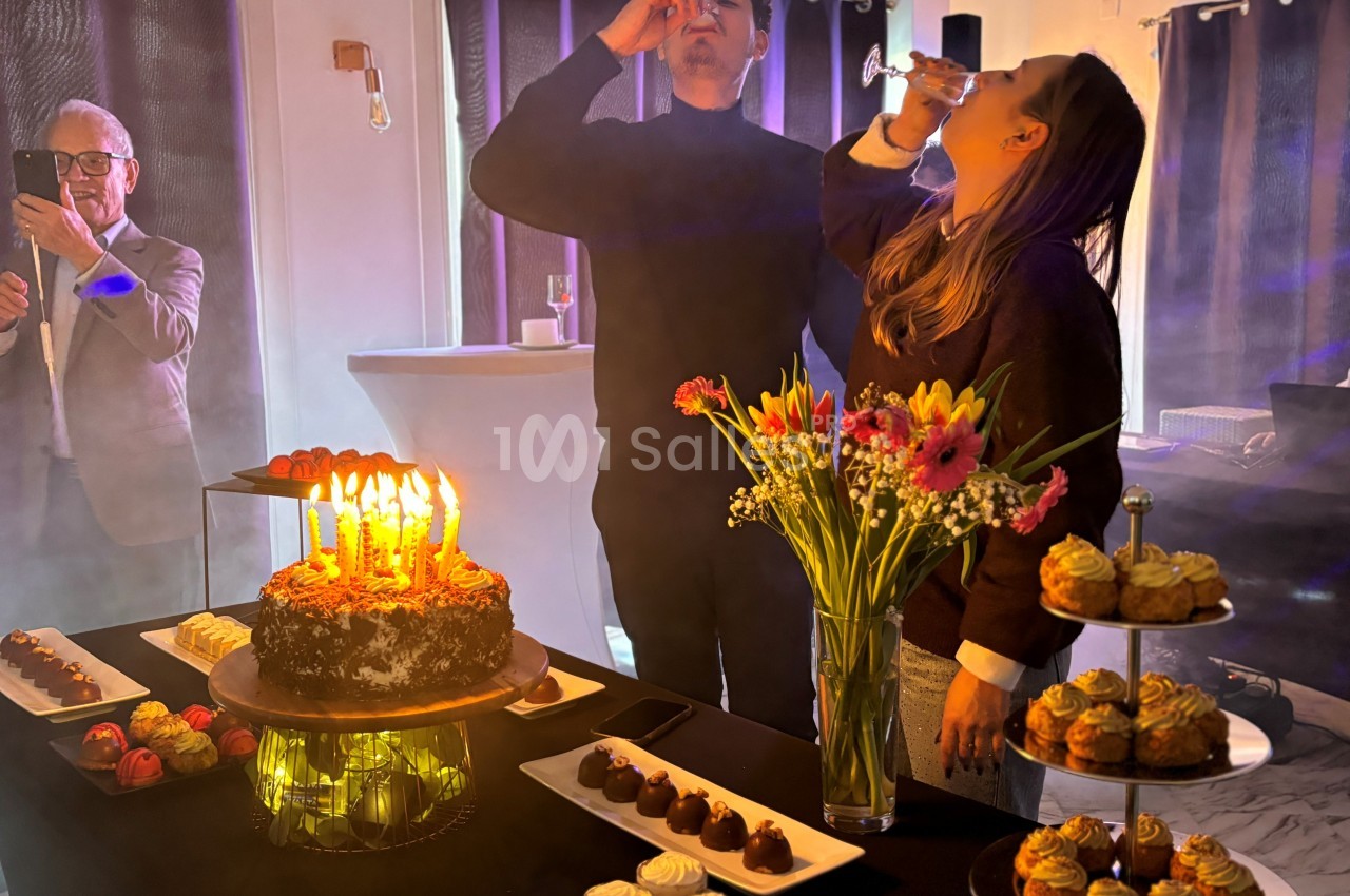 Deux personnes trinquent près d'une table garnie de desserts et d'un gâteau d'anniversaire avec des bougies allumées.