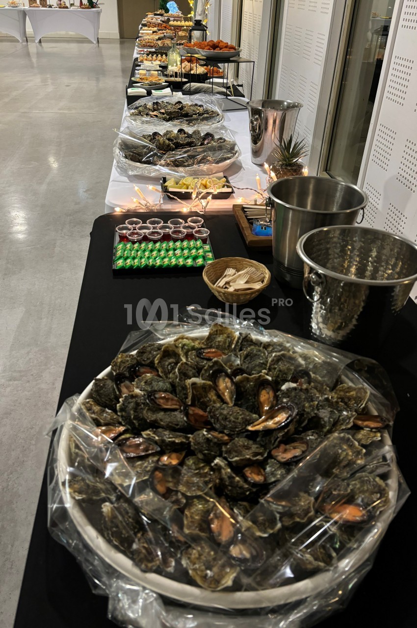 Buffet avec des plateaux d'huîtres, verrines et autres mets disposés sur une longue table dans une salle lumineuse.