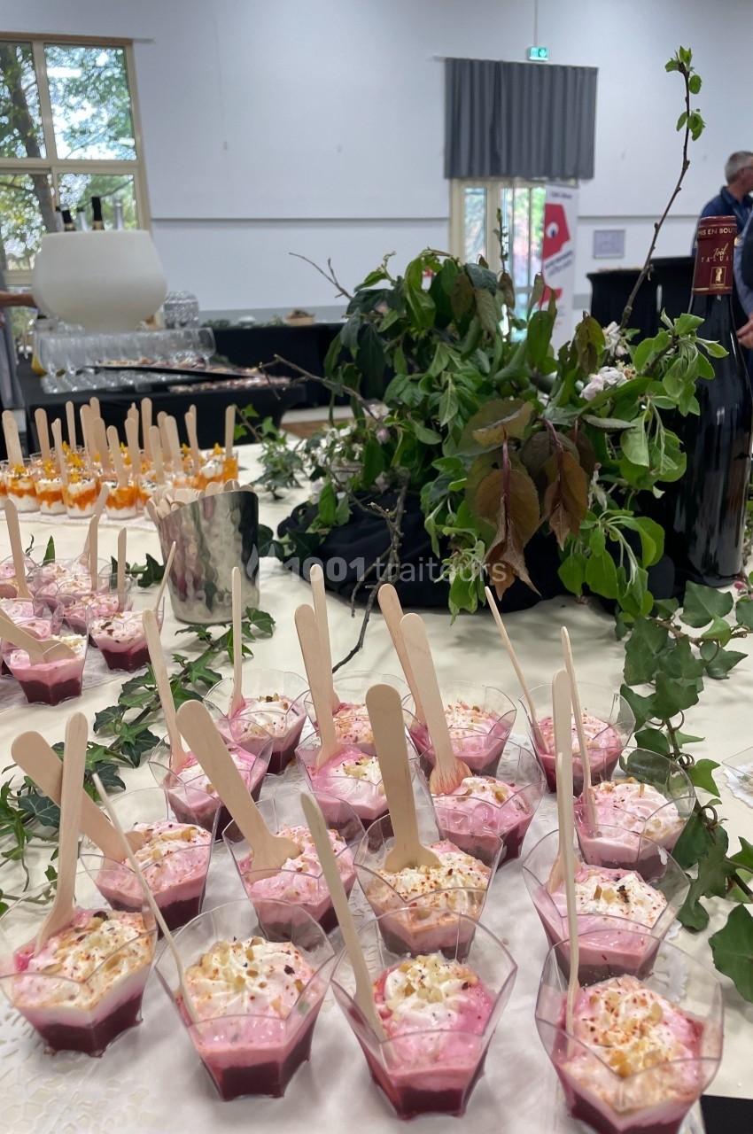 Desserts individuels roses avec cuillères en bois, disposés sur une table décorée de feuillage et de bouteilles de vin.