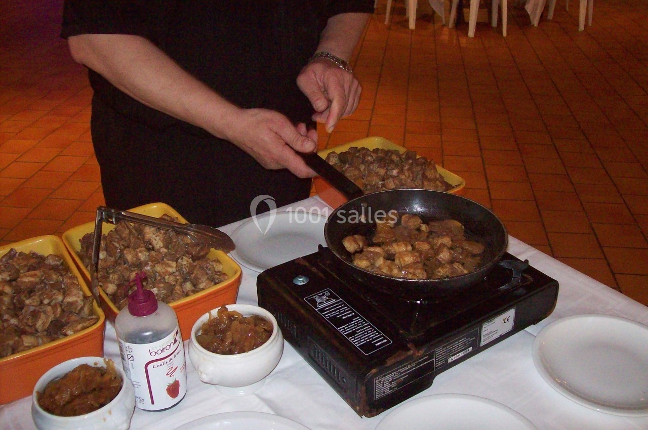 Une personne cuisine des morceaux de viande dans une poêle sur un réchaud, avec des plats et condiments à proximité.