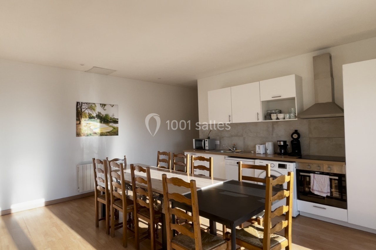 Cuisine lumineuse avec table en bois, chaises assorties, électroménagers modernes et un tableau mural.