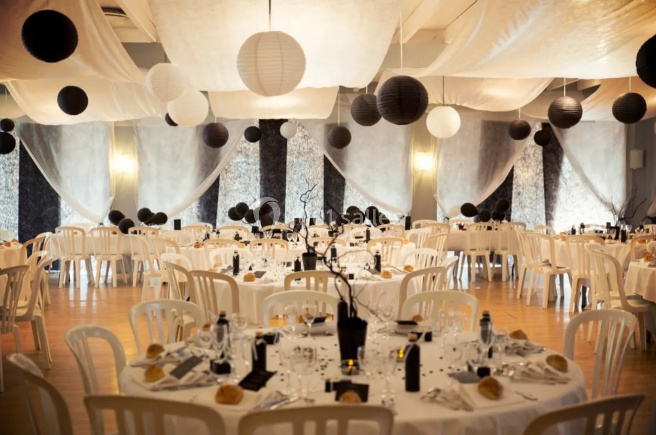 Salle de réception décorée avec des tables rondes, nappes blanches, lanternes noires et blanches suspendues.