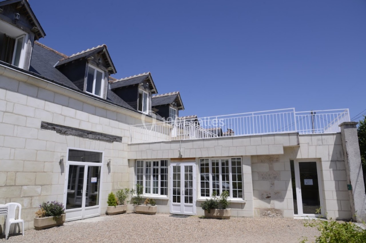 Façade d'une maison en pierre blanche avec des fenêtres à carreaux et une terrasse à garde-corps blanc.