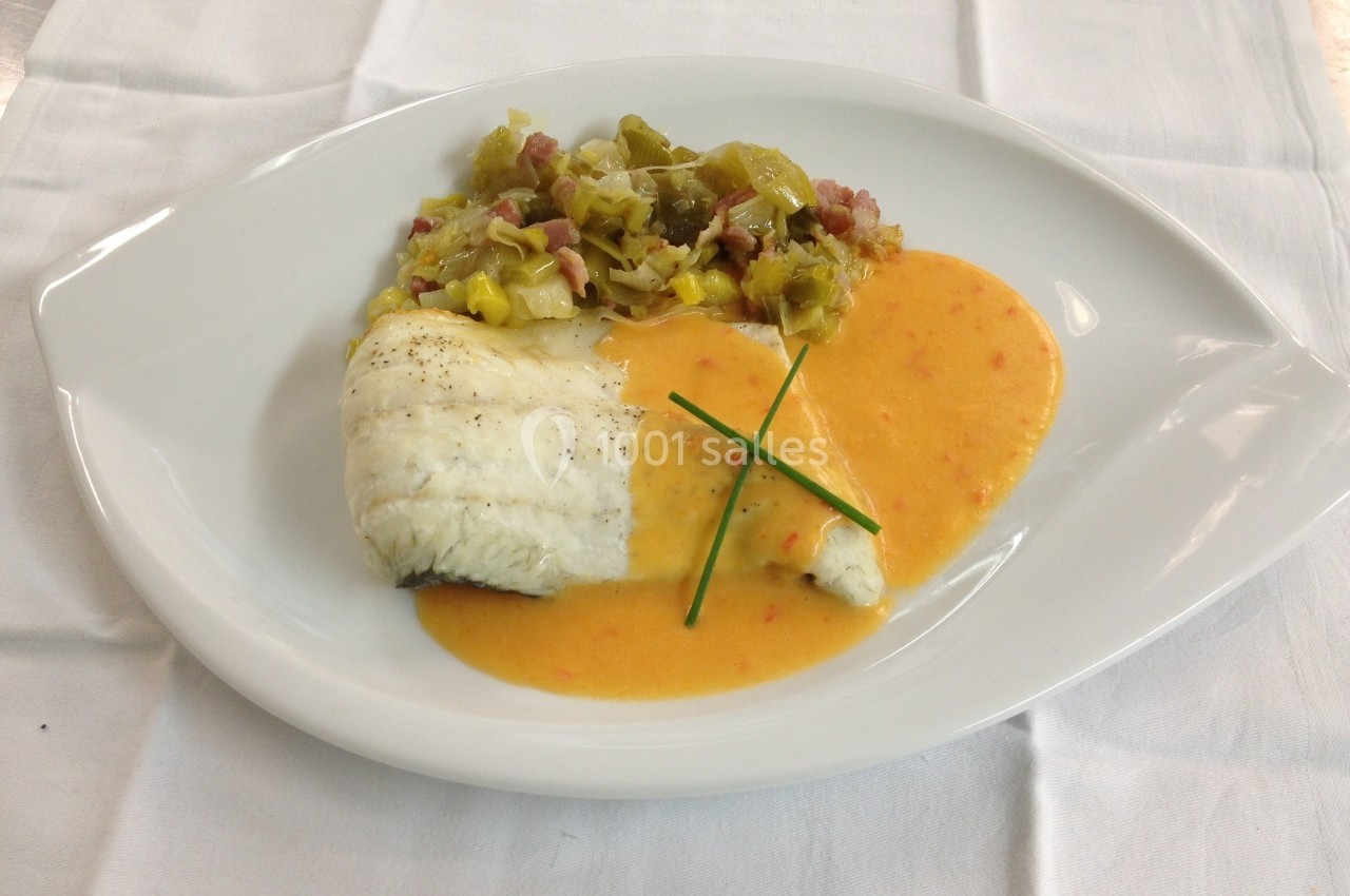 Filet de poisson blanc avec sauce crémeuse orange, accompagné de poireaux et lardons sur une assiette blanche.